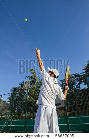 Professional tennis player is doing a kick tennis on a tennis court on a sunny summer morning. He is dressed in sportswear.