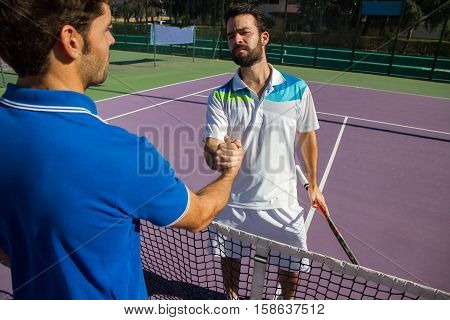 Two men, professional tennis players shake hands before and after the tennis match. One of they has the face of anger. He is trying to intimidate his opponent.