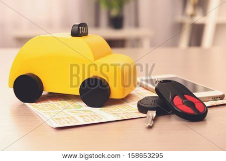 Yellow toy taxi, smartphone, car key and map on wooden table
