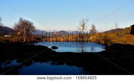 A small lake next to the rock with nice clear blue sky and some trees around.