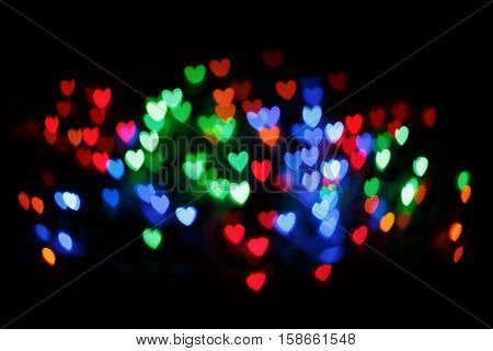 Bright colorful heart bokeh background. Multicolored blurry hearts on a black background.