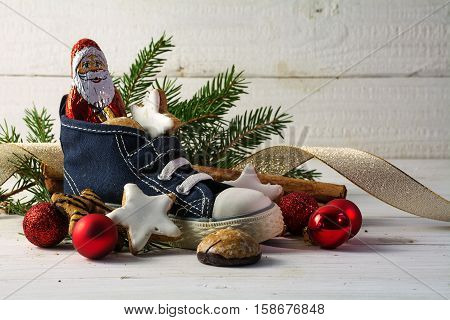 Childrens shoes filled with sweets cookies and christmas decoration for Nicholas day on the 6th December in Germany in front of white rustic wood with copy space selective focus narrow depth of field
