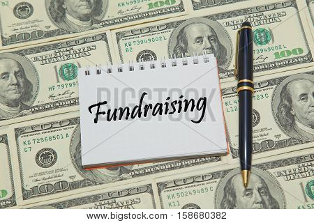 Notebook page with words FUNDRAISING on dollar background