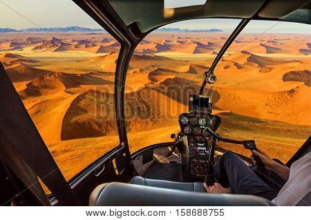Helicopter cockpit flies in Dead Valley, Sossusvlei desert in Namib Naukluft National Park, Namibia, with pilot arm and control board inside the cabin.