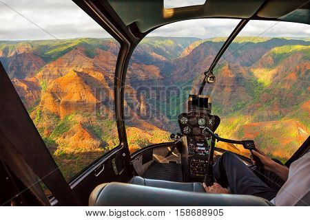 Helicopter cockpit flies in colorful Waimea Canyon State Park, also called Grand Canyon of Pacific, at sunset in Kauai, Hawaii, United States, with pilot arm and control board inside the cabin.