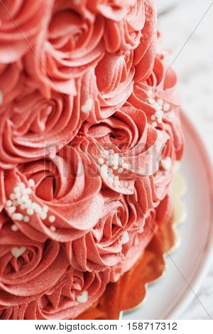 Gorgeous two-tier cake covered in roses made of butter cream icing sitting on a cake pedestal with background