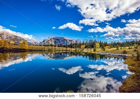 The concept of recreational tourism. Bright shining autumn day in Canmore, near Banff National Park. Majestic mountains and scenic cumulus clouds are reflected in the lake