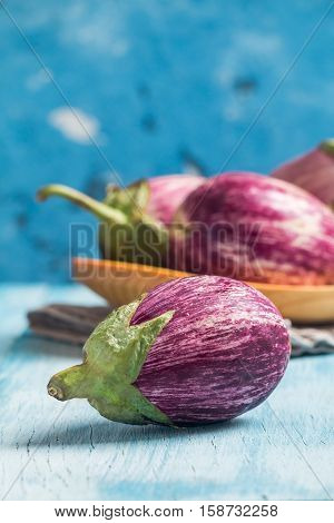 Eggplant varieties in wooden bowl over blue  background.