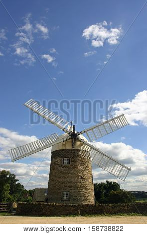 Heage windmill in Derbyshire from the front showing the cap and four out of the six sails (two missing) with a background of blue and grey sky with white clouds.