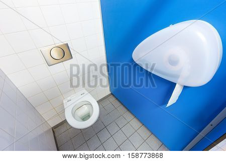 Toilet with paper holder and white wall with tiles