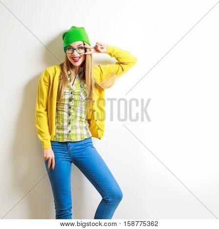 Funny Hipster Girl at White Wall Background. Street Syle Teenage Girl Smiling and Going Crazy. Trendy Casual Female Fashion Outfit in Spring or Autumn. Not Isolated Photo with Copy Space.