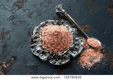 Special pink Adygei salt with spices (Russia) in glass plate and spoon on a dark textured background. Prepared according to the old recipe with garlic and spices. Useful economically spent