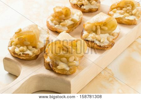 Canape or crostini with toasted baguette ricotta cheese pears nuts Siberian pine and honey on a wooden board. Ideal as an aperitif. Selective focus