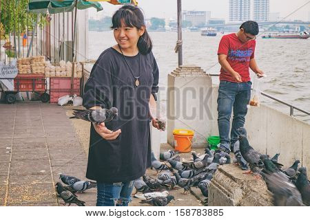Bangkok, Thailand - January 8, 2016: Thai girl and boy smiling and feeding pigeons on the waterfront of Wat Rakhang Pier, Bangkok, Thailand. Here is the famous Wat Rakhang Girls' School.