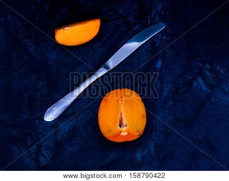 Ripe persimmons on a dark background, divided with a knife. cut off let