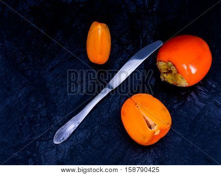 Ripe persimmons on a dark background, divided with a knife. cut off let