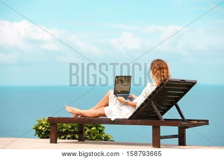Beautiful Business Woman Working Online On Laptop Computer While Lying On Beach Lounger. Relaxing And Using Notebook For Freelance Internet Work. Communication Technology