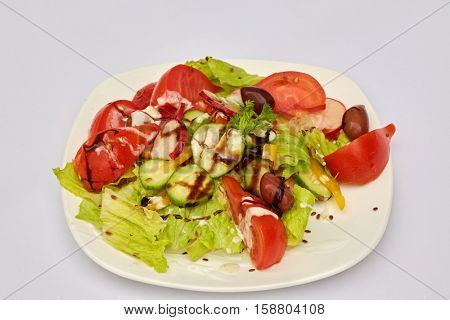 Plate with salad of tomato, cucumber, olives and lettuce leaves.