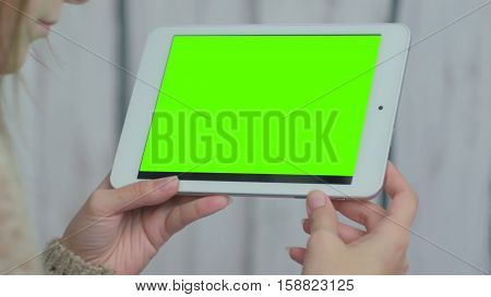 Woman looking at horizontal tablet computer with green screen. Close up shot of woman's hands with pad. White wooden background