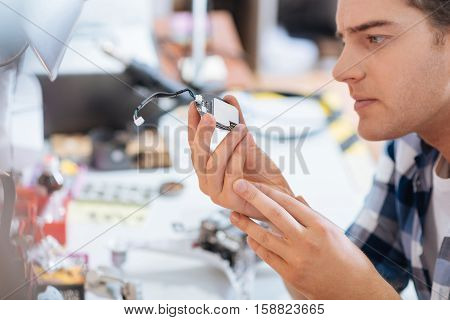 Under control. Serious smart concentrated man discovering chip of a drone attentively while repairing it and spending time in a workroom.
