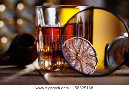 Glass of whiskey, magnifying glass, lemon and smooking pipe