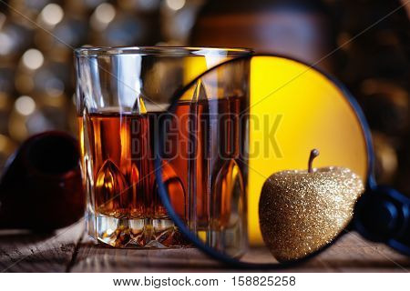 Glass of whiskey, magnifying glass, golden apple and smooking pipe
