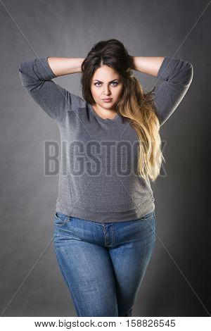 Young beautiful plus size model in blue jeans xxl woman on gray studio background
