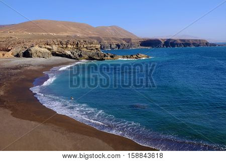 View on the beach Playa de Ajuy with a single person enjoying the ocean on the Canary island Fuerteventura Spain.