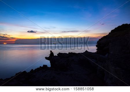 Women siting on a ledge of a mountain enjoying the beautiful sunset over a wide river valley in Thailand
