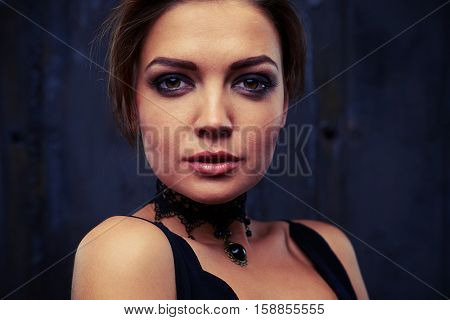 Side portrait of classy elegant woman in black eveningwear who is looking down and posing in dark studio background 