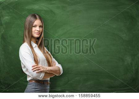 Young businesswoman with his arms across on green chalkboard background. Daily planning. Time-management. Secretary work.