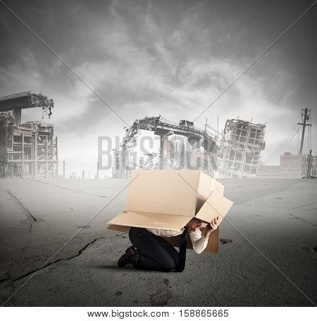 Afraid businessman is hiding under a cardboard in a city destroyed