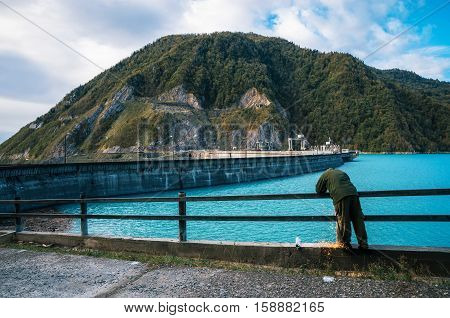 Industrial worker man carries repair maintenance work using arc welding on metal construction on the Enguri hydroelectric dam HES next to Jvari Reservoir with beautiful turquoise water against the mount Upper Svaneti Georgia