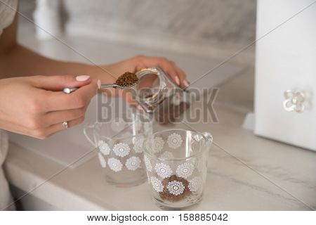 Hand with full spoon and glasses preparing instant coffee