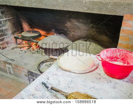 Picture of the stone bread oven stove with burning wood fire and red flames inside. lurred image of the red pot on the table with water-logged dough.