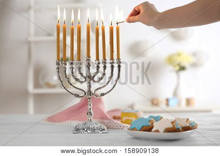 Female hand applying match to candles in menorah on wooden table. Hanukkah concept