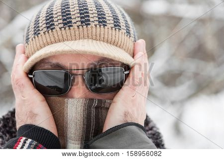 Portrait of an adult man in knitted cap scarf and sunglasses outdoors in winter day closeup
