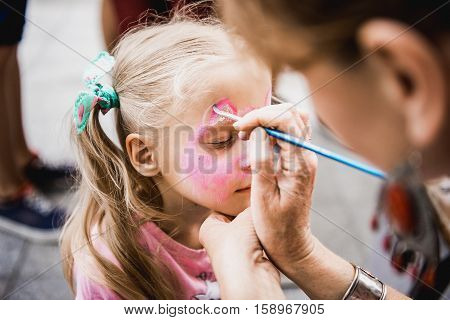 woman painting face of kid outdoors. baby face painting