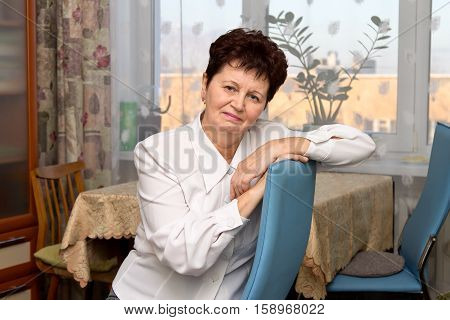 Positive elderly woman posing leaning back in the chair at home