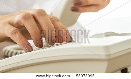Woman with varnished nails dialling on a land line telephone instrument in a close up view conceptual of business and communication.