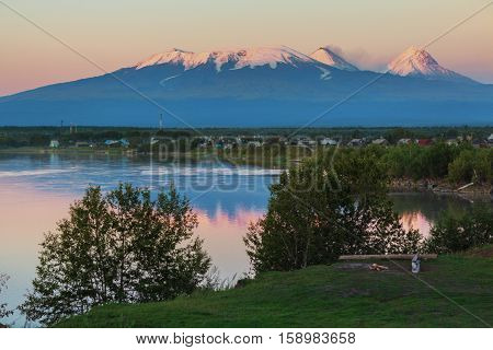 Sunset lighting Kluchevskaya group of volcanoes with reflection in the river Kamchatka.