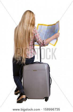 back view of woman traveler sitting on their suitcases and looking for a route map. backside view of person. Isolated over white background. Long-haired girl sitting on a suitcase and looking at map.