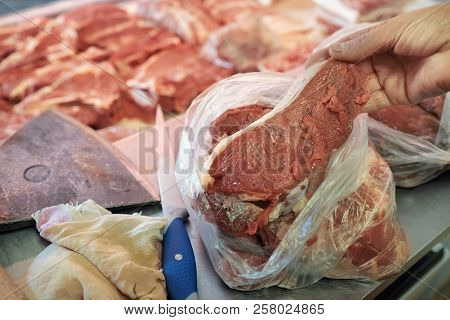 Ax, Knife And A Butcher Hand Holding A Piece Of Raw Meat Displayed In A Butcher Shop