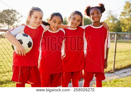 Four young girls in football strip looking to camera smiling