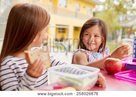 Two young schoolgirls eating packed lunch looking each other