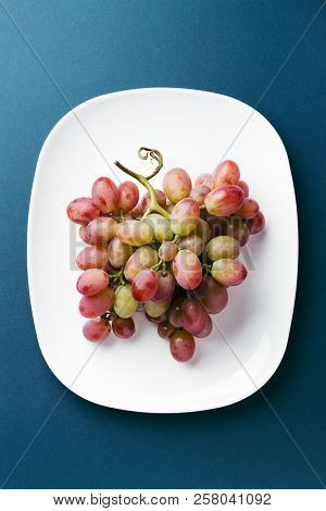 Bunch Of Red Grape On White Plate On Dark Blue Background. Top View.