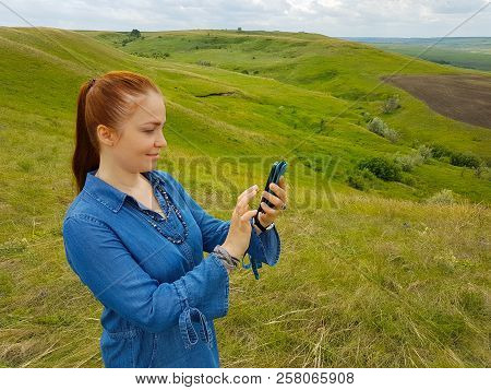 A Young Woman With Red Hair And A Blue Denim Dress Is In The Mountains Outside The City And Is Tryin