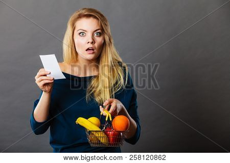 Shocked Woman Holding Shopping Basket With Fruits Looking At Bill Receipt Being Scared Of Huge Price