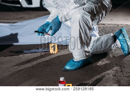 Cropped Image Of Criminologist In Latex Gloves And Protective Suit Holding Knife Above Blood On Grou