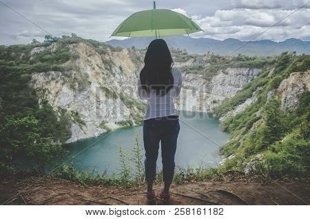 Hipster Young Girl With Green Umbella Enjoying Sunset On Peak Mountain. Tourist Traveler On Backgrou